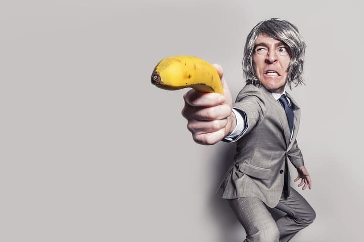 Um senhor branco furioso de cabelo cinzento e um fato formal cinzento segurando uma arma de banana